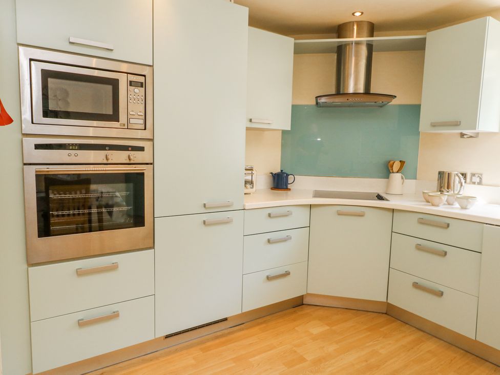 A kitchen with built in microwave oven and oven white cabinets and blue glass backsplash at 6 Red Sails in Sandbanks