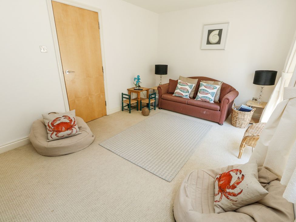 A living room with a sofa cushions with fish patterns small table and chairs and cushions with crab patterns at 6 Red Sails in Sandbanks
