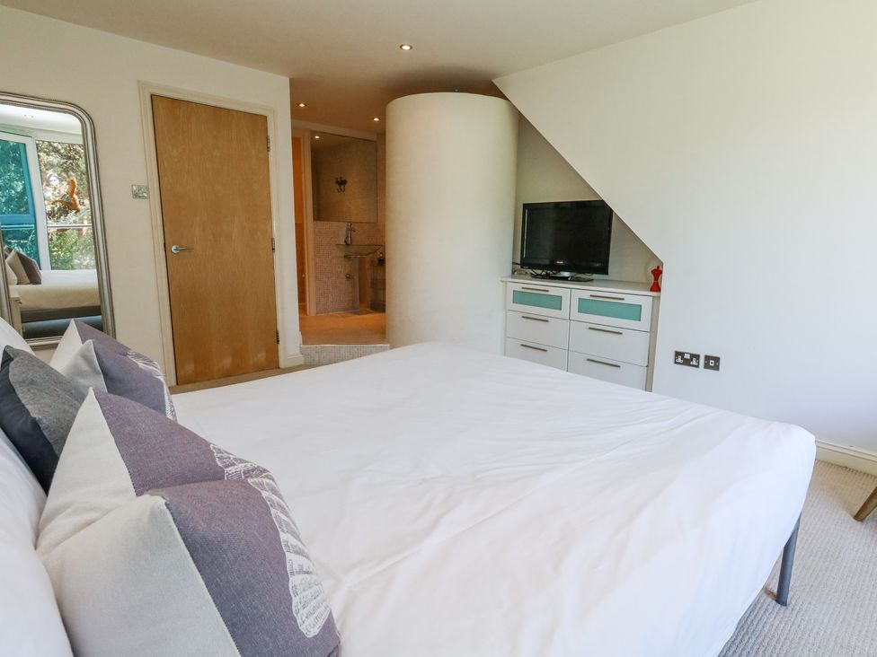 A bedroom with a bed and pillows a chest of drawers with a television on top and a door leading to a bathroom at 6 Red Sails in Sandbanks