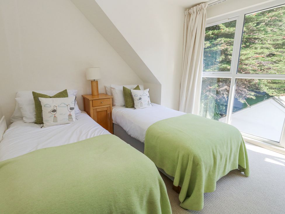 A bedroom with two single beds green blankets and a wooden nightstand with a lamp near a window at 6 Red Sails in Sandbanks