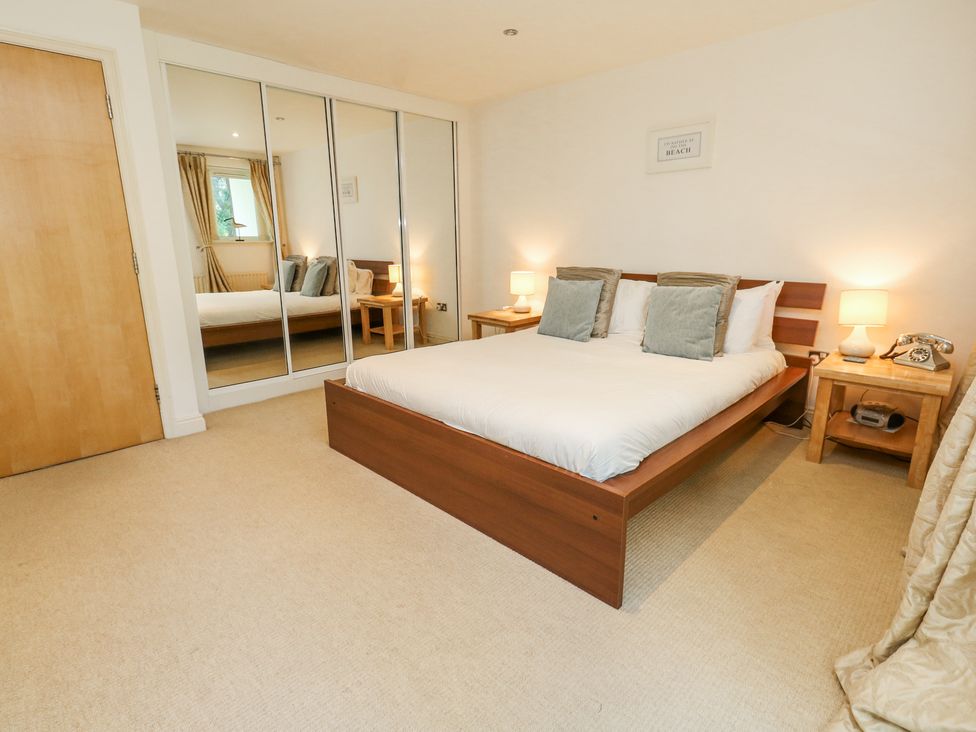 A bedroom with a wooden bed, two side tables with lamps, mirrored wardrobe doors, and a carpeted floor at 6 Red Sails in Sandbanks