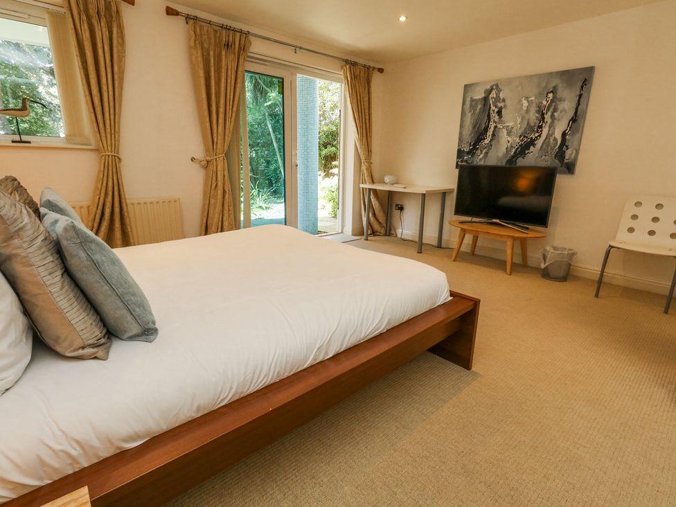 A bedroom with a bed cushions television on table and glass doors with curtains at 6 Red Sails in Sandbanks