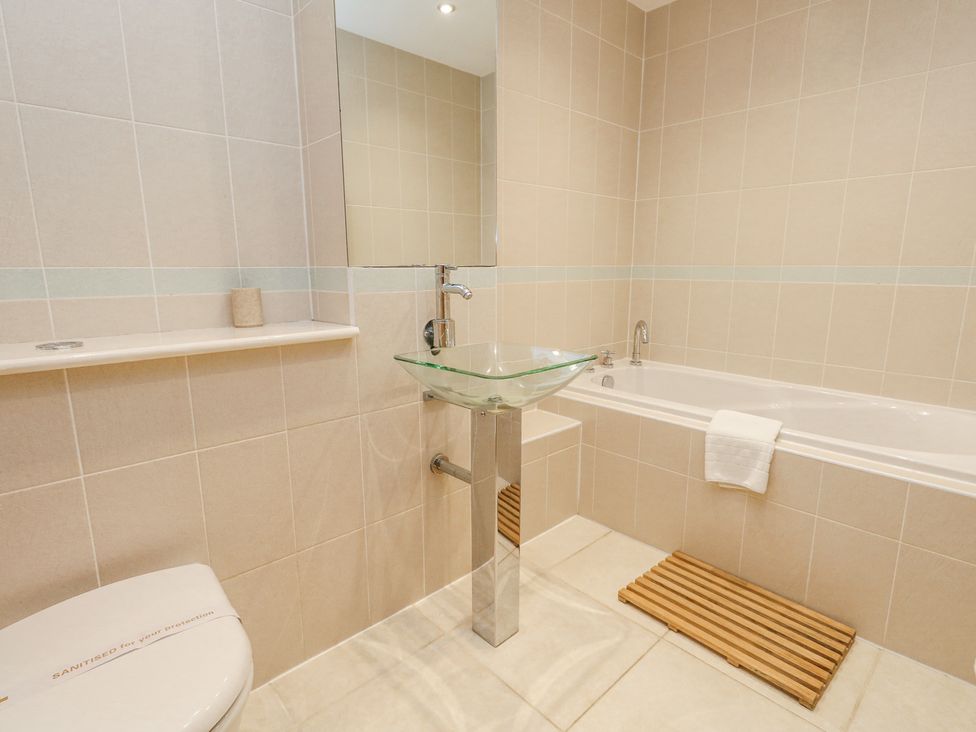 A bathroom with a glass sink on a metal pedestal bathtub with a towel and wooden mat on the floor at 6 Red Sails in Sandbanks