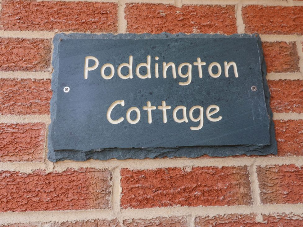 A slate sign reading Poddington Cottage on a brick wall