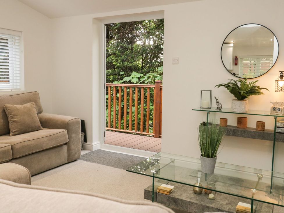 A living room with brown sofa a glass table plants and an open door to a wooden deck at Mere Brook Lodge in White Cross Bay