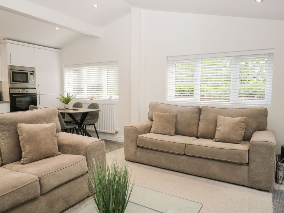 A living room with two beige sofas and a small dining table with chairs near a kitchen at Mere Brook Lodge in White Cross Bay