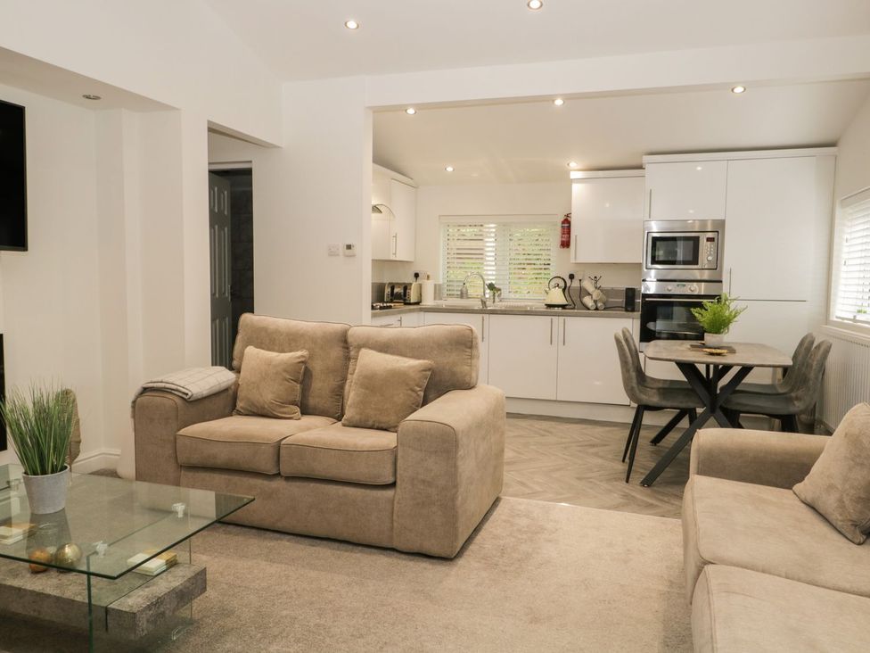 An open living room and kitchen with beige sofas glass coffee table dining table and white cabinets at Mere Brook Lodge in White Cross Bay
