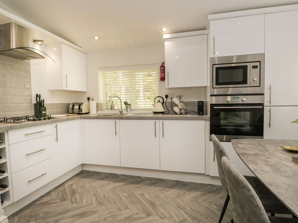 A modern kitchen with white cabinets a gas stove built in microwave and oven a sink under a window and a dining table with chairs at Mere Brook Lodge in White Cross Bay