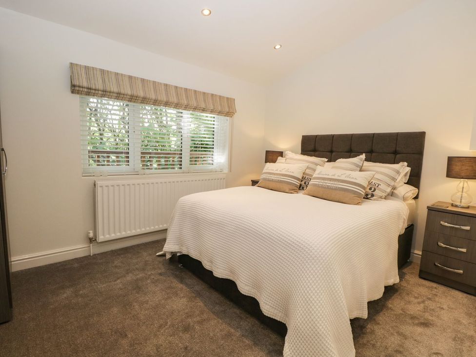 A bedroom with a double bed with pillows bedside tables with lamps and a window with blinds at Mere Brook Lodge White Cross Bay