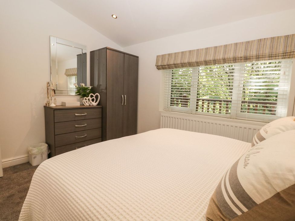 A bedroom with a bed white bedding a gray wardrobe and chest of drawers with a mirror and window blinds at Mere Brook Lodge White Cross Bay