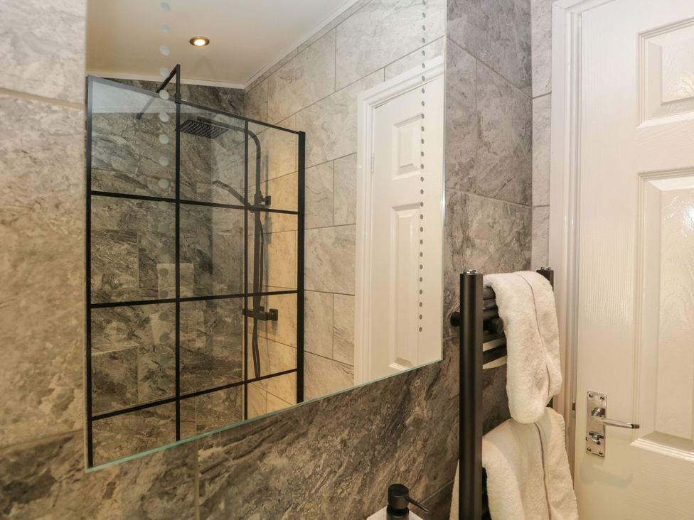 A bathroom with a glass shower enclosure a black towel rack with white towels and a white door at Mere Brook Lodge in White Cross Bay