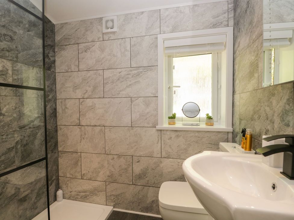 A bathroom with a shower enclosure, toilet, sink, and a window with small plants and a mirror on the sill at Mere Brook Lodge in White Cross Bay