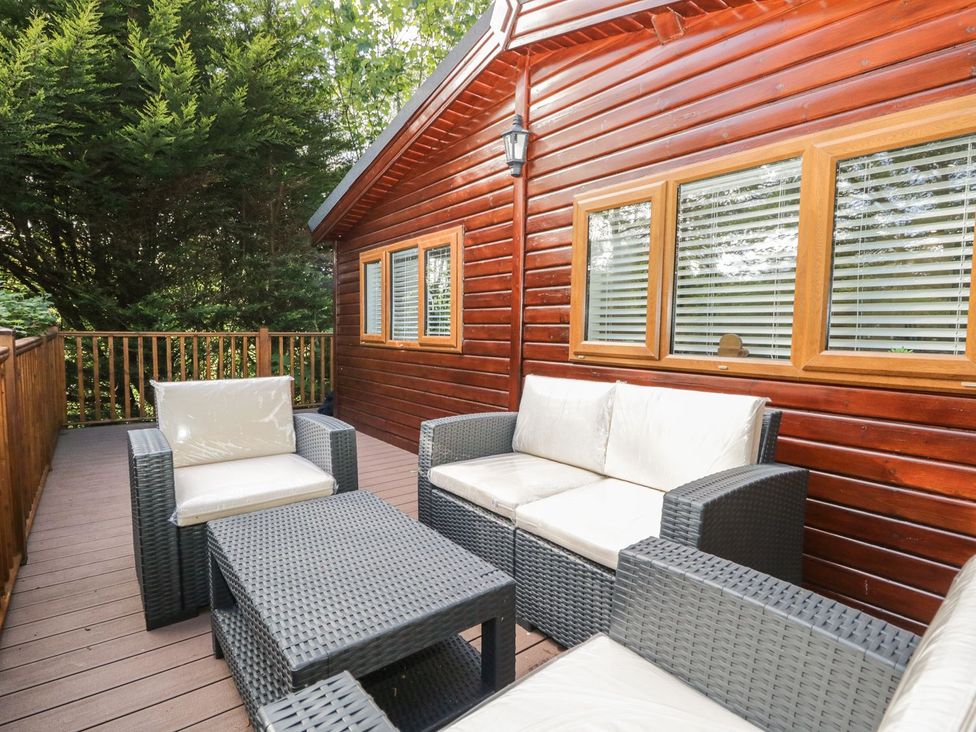 An outdoor deck with wicker furniture and cushions next to a wooden cabin at Mere Brook Lodge in White Cross Bay