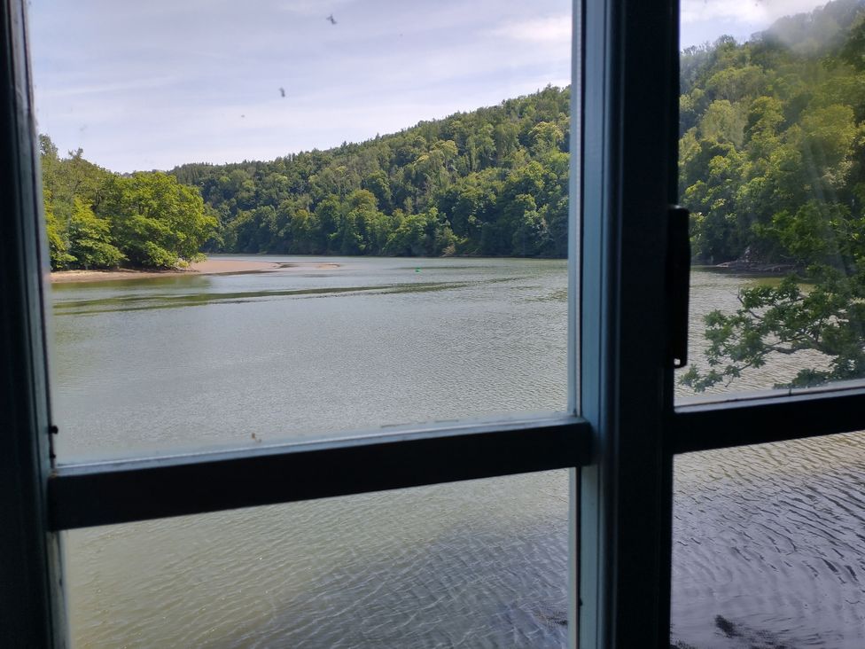 A view from a window overlooking water and trees at The Sharpham Boat House in Ashprington