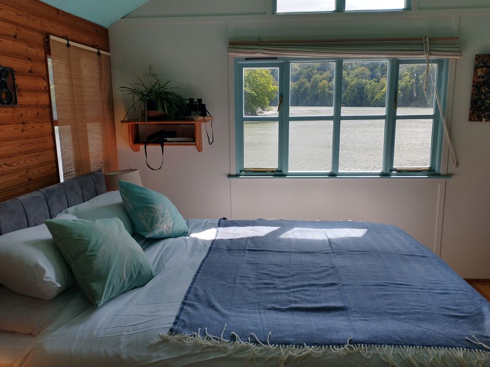 A bedroom with a bed and a window overlooking the water at The Sharpham Boat House in Ashprington