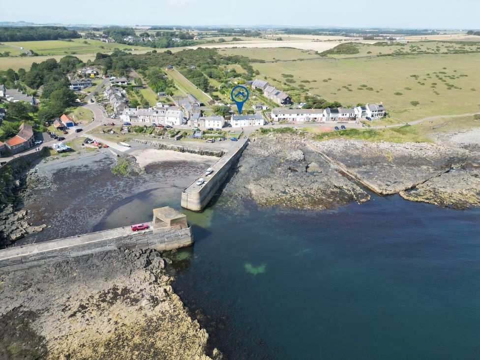 An aerial view of a village near the coast with a pier and parked vehicles at Puffin Cottage in Craster