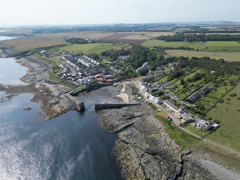 An aerial view of a coastal village with fields and a pier at Puffin Cottage in Craster