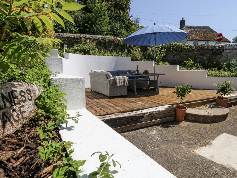 A garden area with sofa, table, umbrella, and potted plants at Happiness Cottage in Piddlehinton