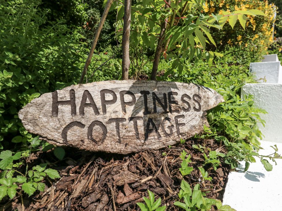 A wooden sign that reads Happiness Cottage in a garden at Happiness Cottage Piddlehinton
