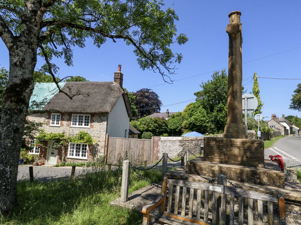 A house with a thatched roof and a memorial in front at Happiness Cottage in Piddlehinton
