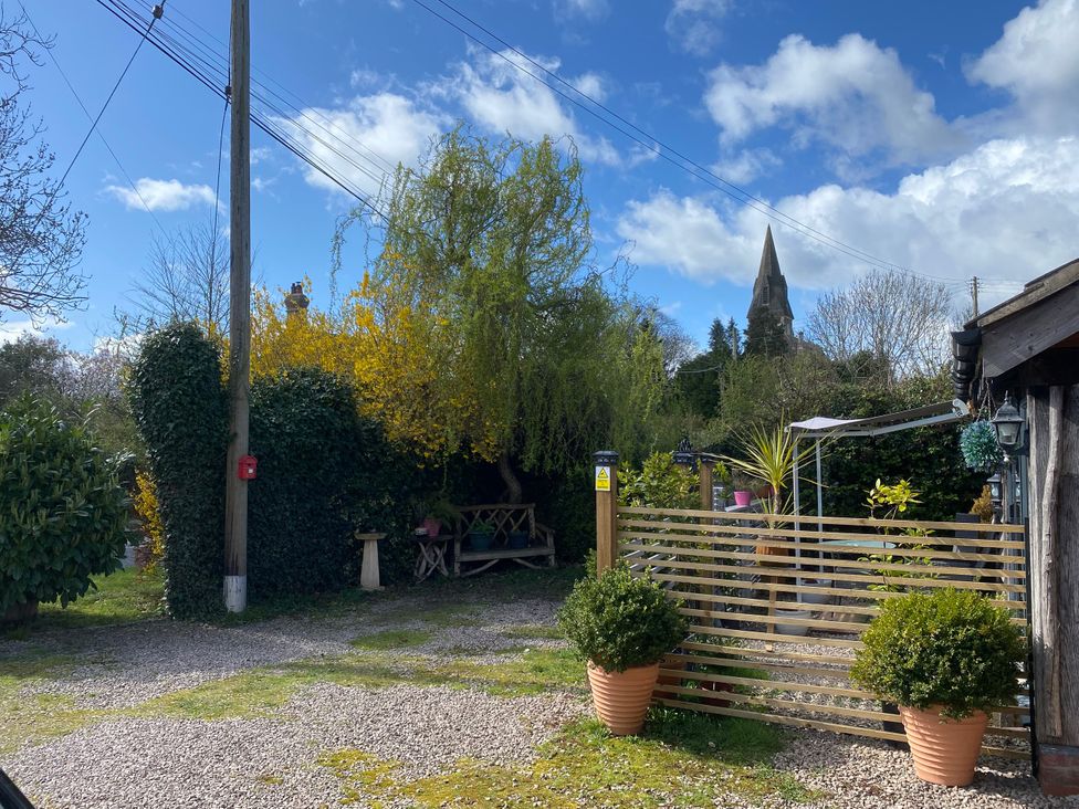 An outdoor area with gravel, fence, potted plants, and church in the background at The Pheasant's Nest near Welland Upton Upon Severn