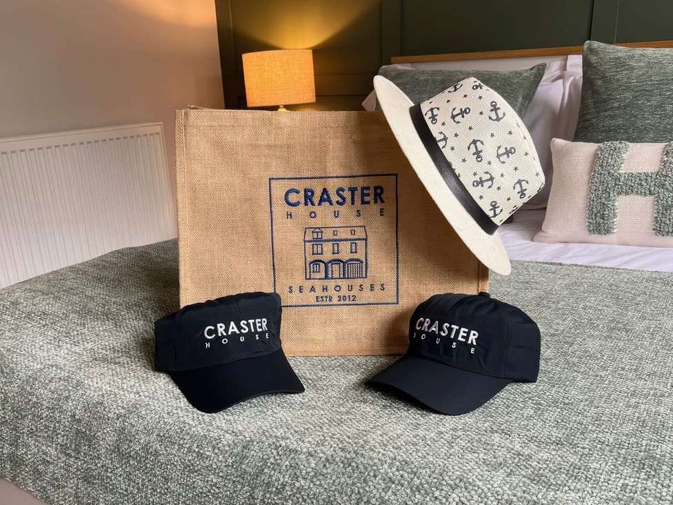 A hat and caps with a bag on a bed at Craster House Seahouses