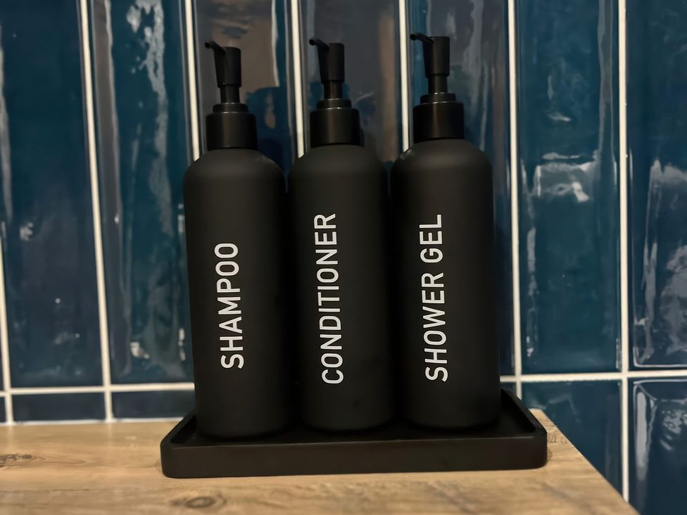 Bottles of shampoo, conditioner, and shower gel on a tray in a bathroom at Craster House in Seahouses