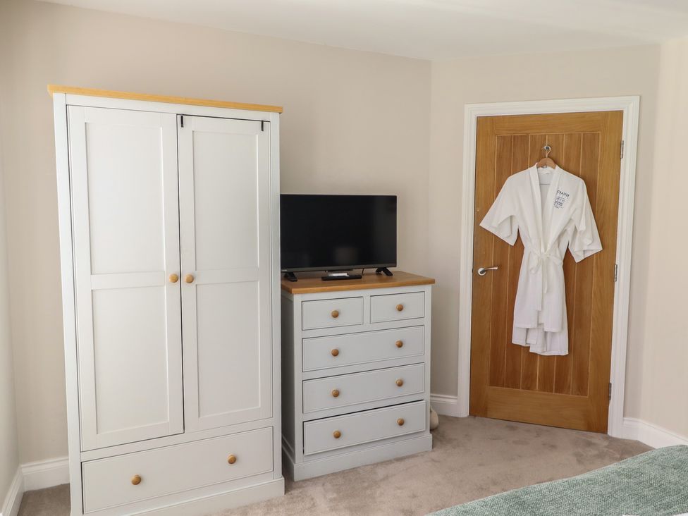 A bedroom with a wardrobe, television, drawer unit, and a dressing gown at Craster House in Seahouses