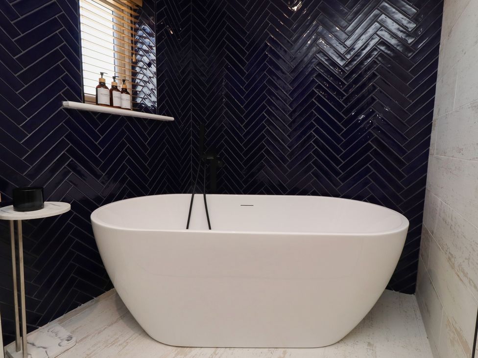 A bathroom with a bathtub and bottles on a shelf at Craster House, Seahouses