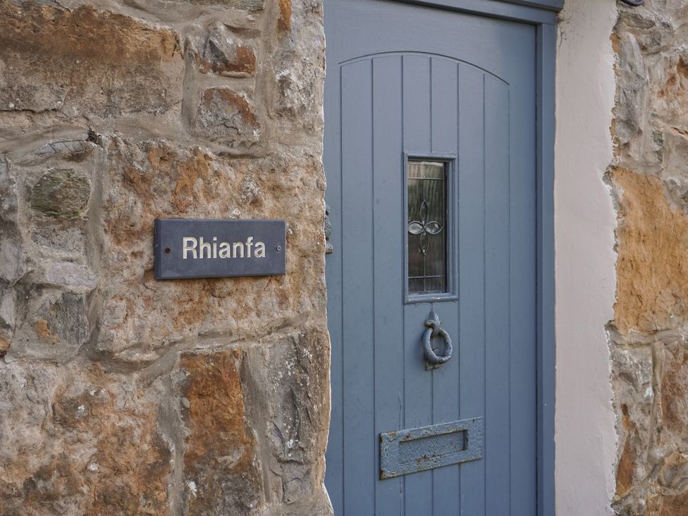 A front door with a stone wall and a sign at Rhianfa in Newborough