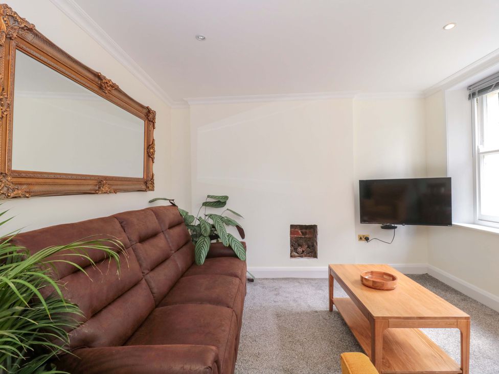 A living room with a sofa, a mirror, a television, and a coffee table at Flat 2 Battledown Grange, Cheltenham