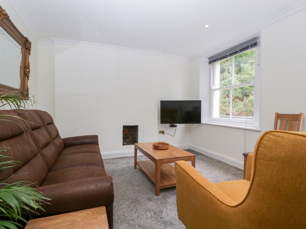 A living room with a sofa, coffee table, television, and chair at Flat 2 Battledown Grange in Cheltenham