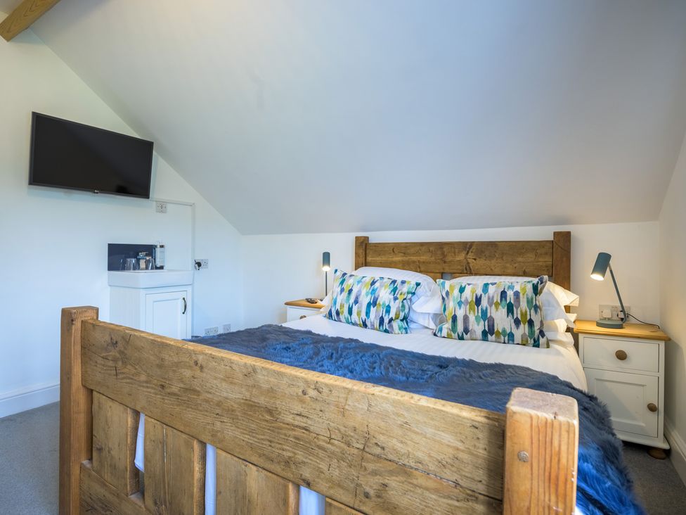 A bedroom with a wooden bed, pillows, and television at Moss Crag in Glenridding