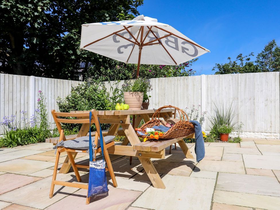 A garden with a table, umbrella, and basket at 15 Llwyn Gwalch Estate Pwllheli