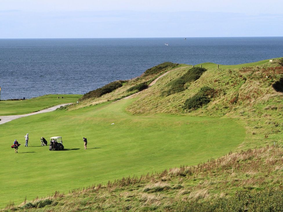 A golf course with golfers and a cart by the sea at 15 Llwyn Gwalch Estate Pwllheli