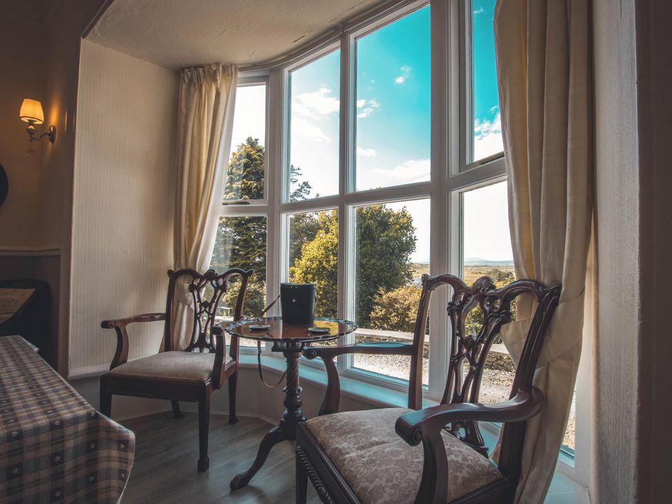 A sitting room with two chairs and a table by a large window at Noddfa Country House Harlech