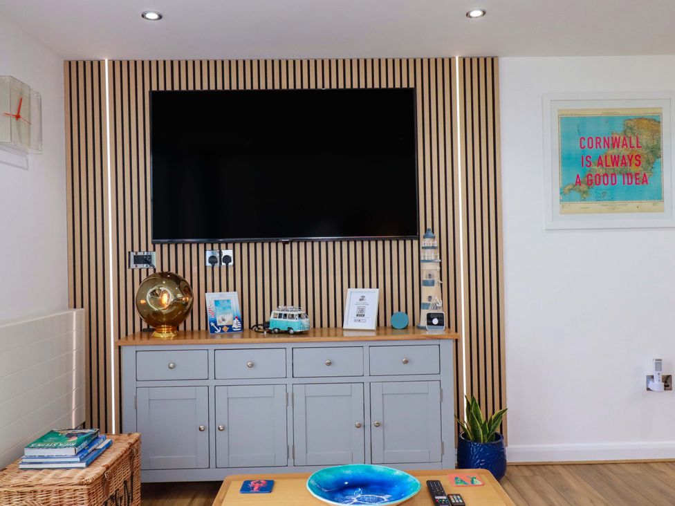 A living room with a television, cabinet, photographs and a decorative globe at Penthouse @46Zinc - Headland View, Newquay