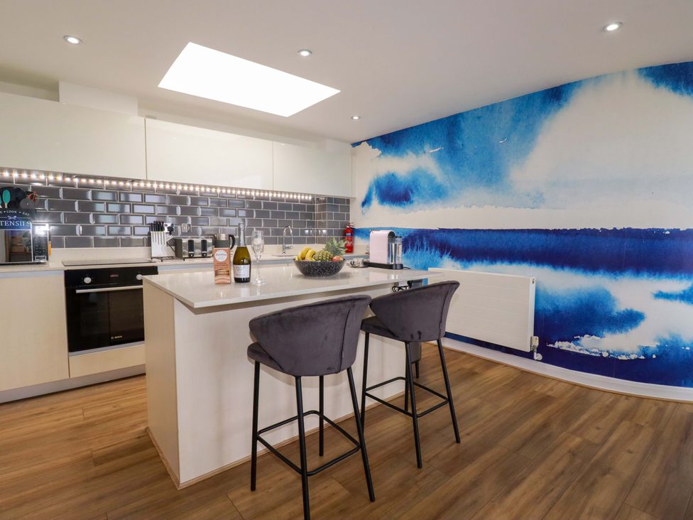 A kitchen with a counter, bar stools, and cooking appliances at Penthouse @46Zinc - Headland View, Newquay