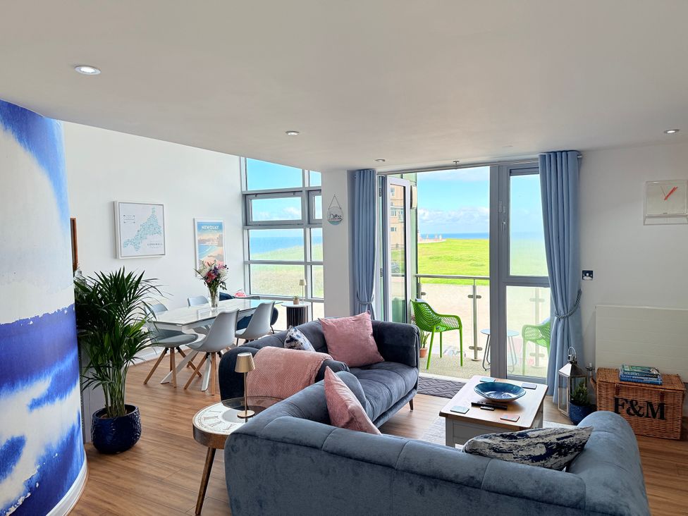 A living room with a sofa, dining table, and large windows at Penthouse @46Zinc - Headland View, Newquay