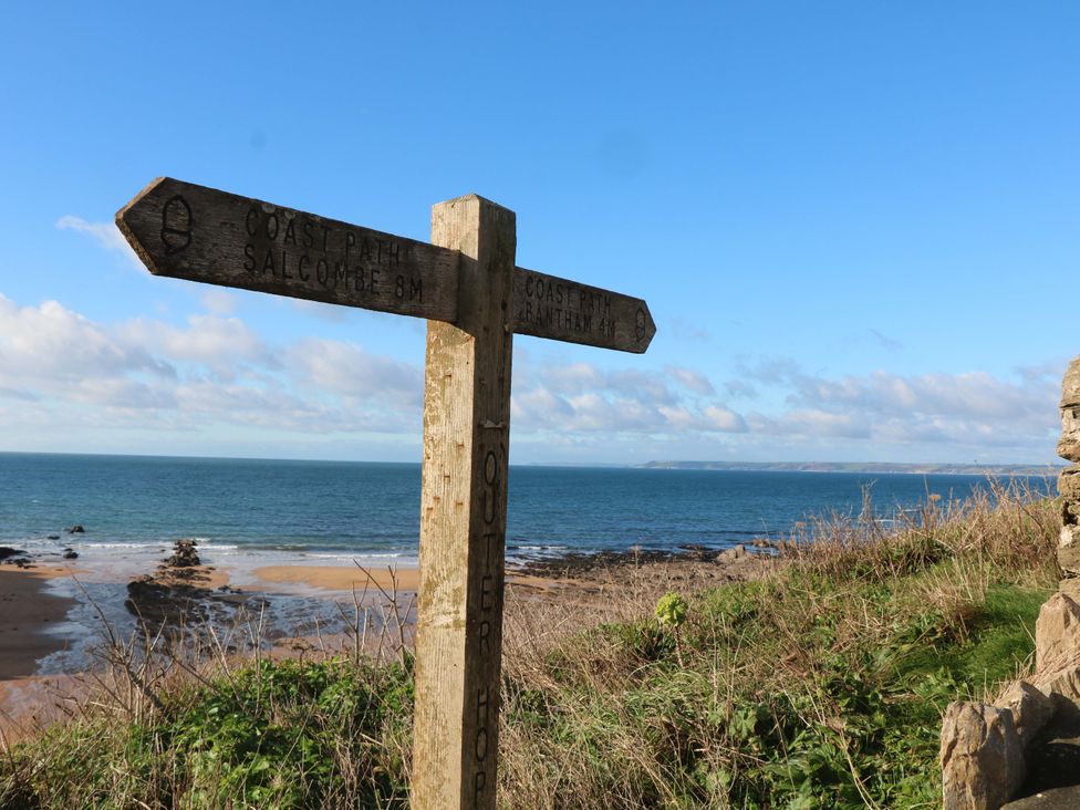 A signpost indicating coast paths to Salcombe and Bantham near the ocean in Hope Cove