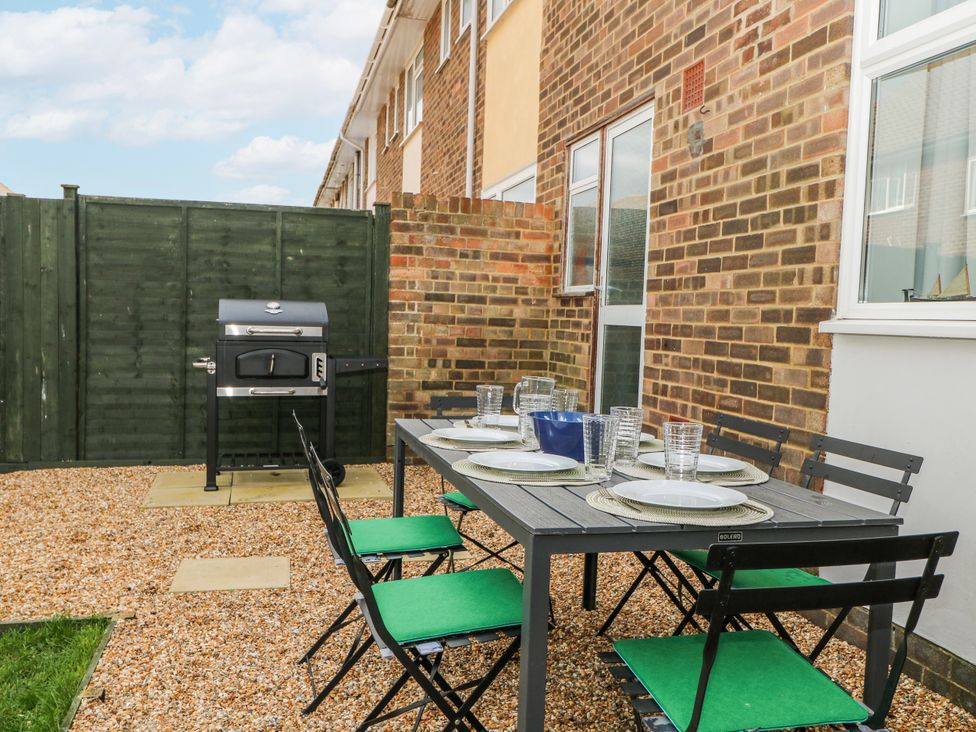 A garden with a table, chairs, and grill at Pebble Place in Rustington
