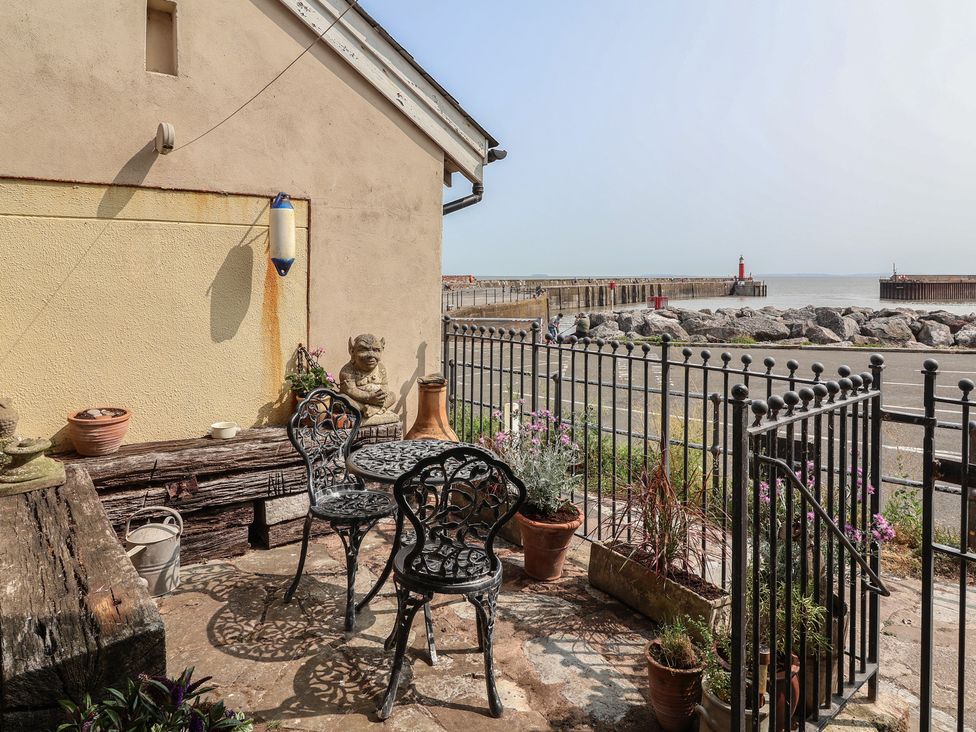 An outdoor patio with chairs and a table overlooking a pier at Sammy Hakes Cottage in Watchet