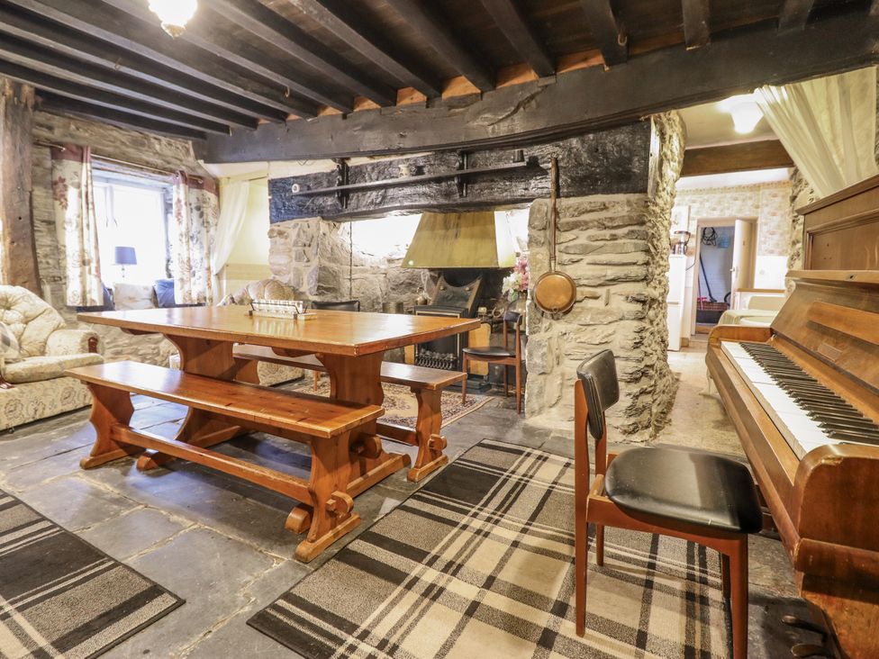 A living room with a table, benches, sofa, and piano at Cynfal Fawr near Blaenau Ffestiniog