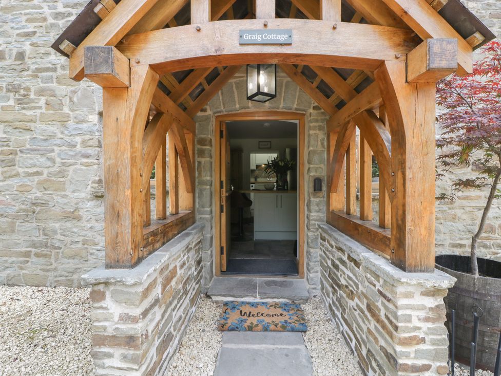 The entrance porch with wooden beams and stone walls showing the open door and a welcome mat at Graig Cottage in Cwmcarn