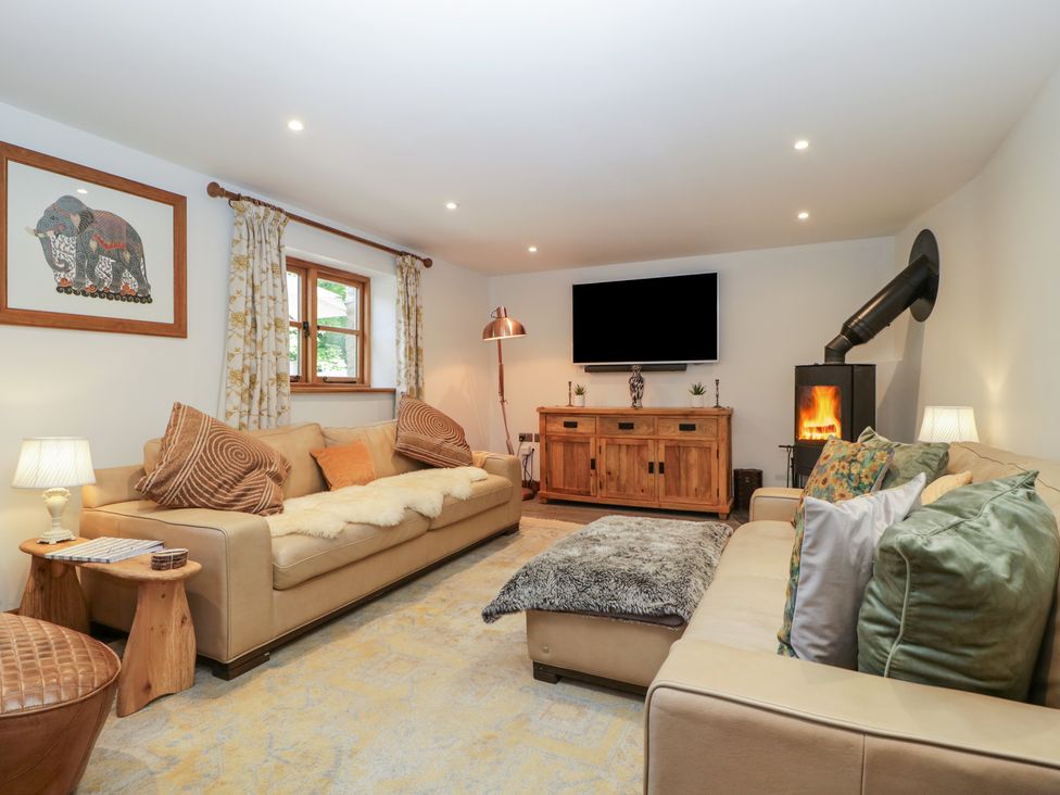 A living room with two sofas a wooden sideboard a wood-burning stove and a wall-mounted television at Graig Cottage in Cwmcarn