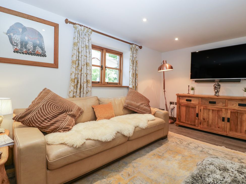 A living room with a leather sofa cushions a wooden TV stand and a large wall mounted TV at Graig Cottage in Cwmcarn