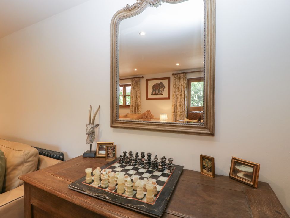 A wooden table with a chessboard and framed pictures underneath a large mirror in a living room at Graig Cottage in Cwmcarn