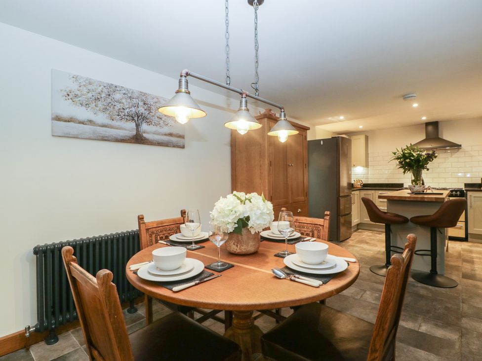 A dining area with a round wooden table set for four and a kitchen with stools at Graig Cottage in Cwmcarn