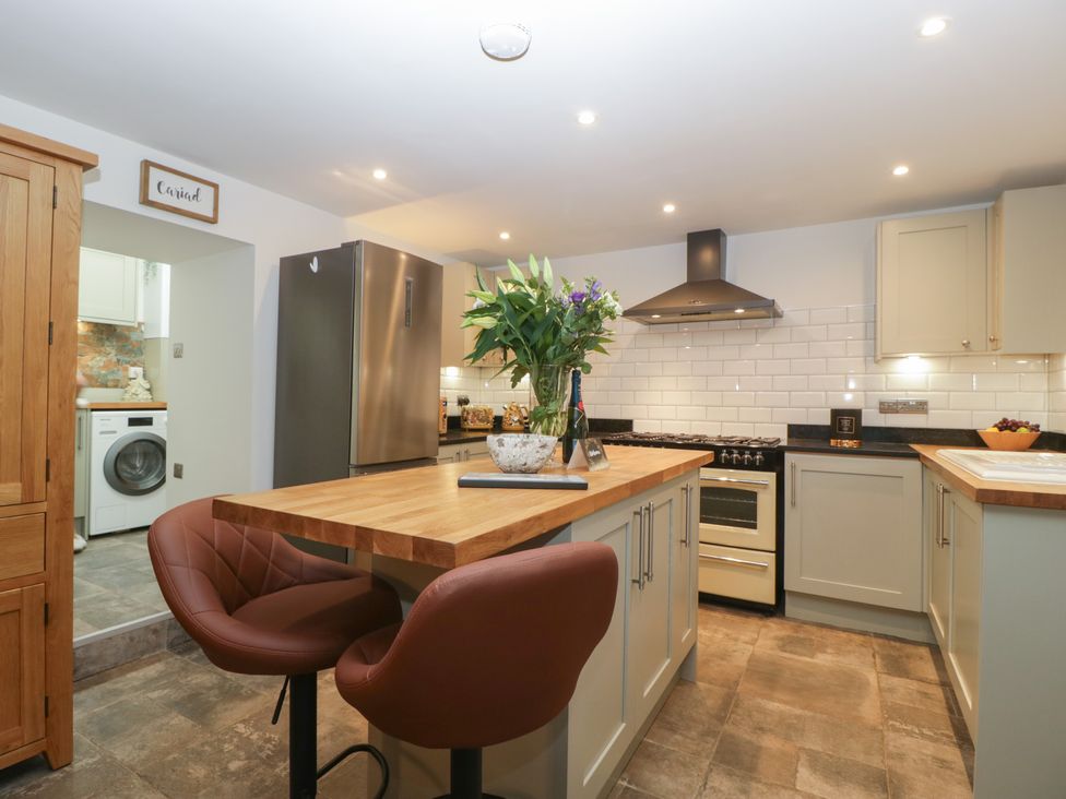 A kitchen with a wooden island, two brown chairs, stainless steel refrigerator, oven, and a washing machine visible through a doorway at Graig Cottage in Cwmcarn