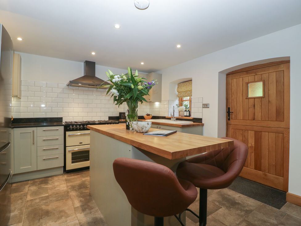 A kitchen with a wooden island and two brown stools near a wooden door at Graig Cottage in Cwmcarn